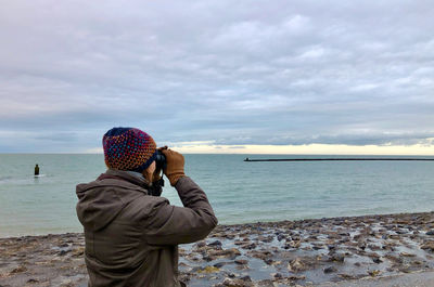 Rear view of woman looking through binoculars while standing at shore