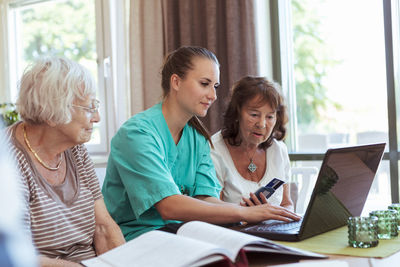 Nurse with senior women buying medicine online using laptop and credit card at nursing home