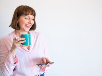 Smiling young woman holding coffee cup against white background