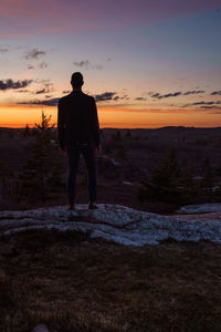 Silhouette man on rock formation against sky during sunset