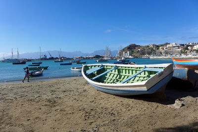 Boats moored on beach against blue sky