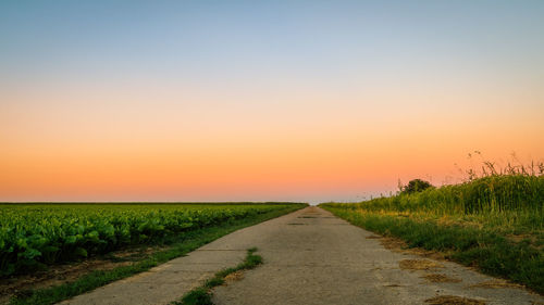 Road amidst field against sky during sunset