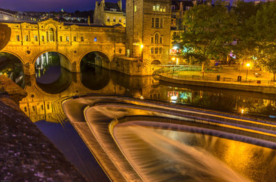 Light trails on bridge over canal in city at night