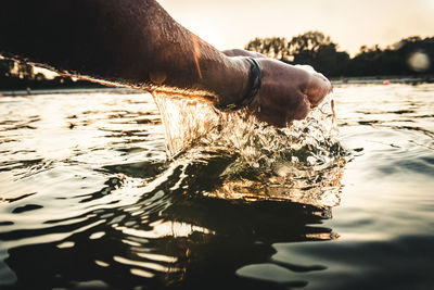 Cropped hands of man splashing water during sunset