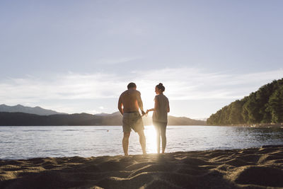 Rear view of couple standing on shore at beach against sky