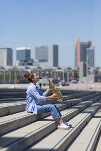 Woman with ponytail playing a saxophone while standing outdoors