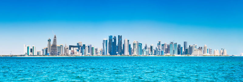 Sea by modern buildings against blue sky