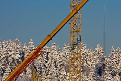 Cranes and snow covered trees against clear blue sky