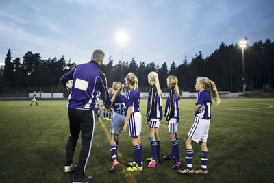 Coach explaining female soccer team on field against sky