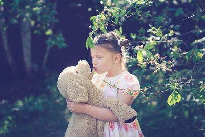 Cute european kid girl in dress with soft big toy dog in backyard, in park summer