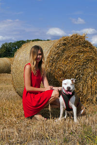 Young woman with dog by hay bale on agricultural field