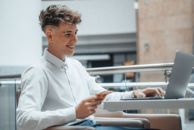 Side view of young man using mobile phone while sitting in office
