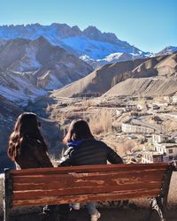 Rear view of people sitting on mountain against clear sky