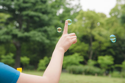 Cropped image of hand holding bubbles against trees