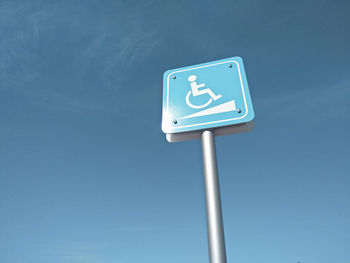 Low angle view of disabled sign against blue sky