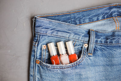 Directly above shot of nail polish bottles in jeans pocket on gray background