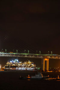 Illuminated bridge over river against sky at night