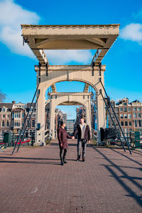 People on bridge in city against sky