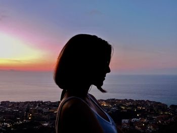 Side view of woman standing against sea during sunset