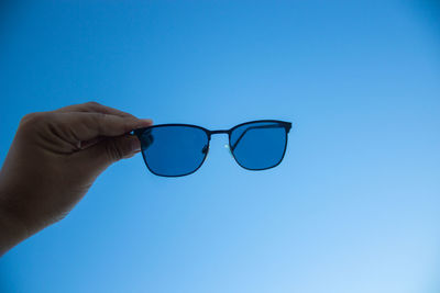 Close-up of hand holding eyeglasses against blue sky