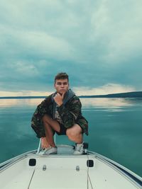 Full length of man crouching on boat over lake against sky