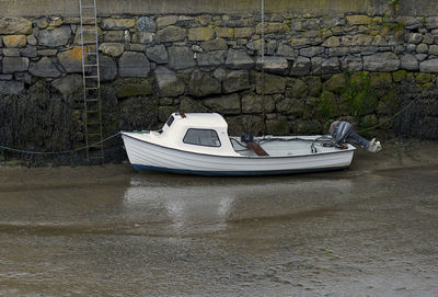 Boat moored on shore against wall