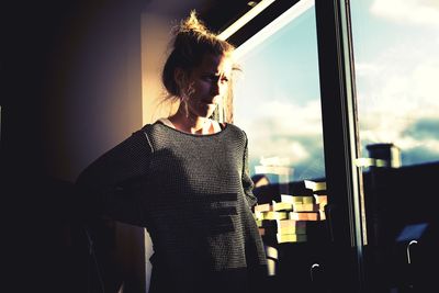 Young woman standing by window against sky