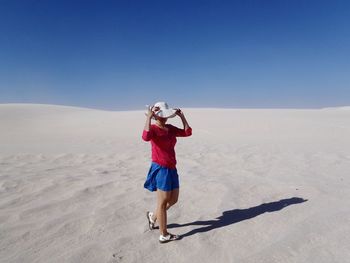 Full length of woman wearing hat while walking on sand at desert