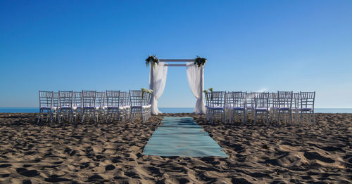  wedding baldachine and chairs on beach against clear blue sky