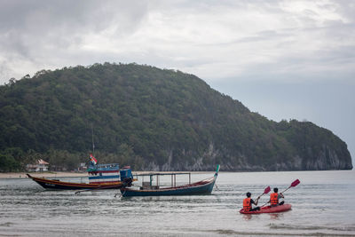 Rear view of people kayaking on sea against sky
