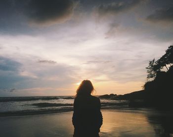 Rear view of woman standing against sea during sunset