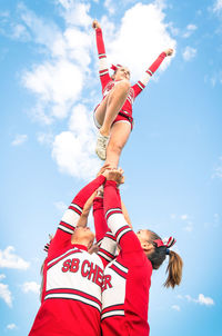 Low angle view of cheerleaders forming pyramid against cloudy sky