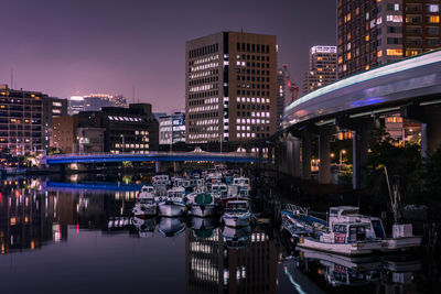 Illuminated buildings by river against sky in city at night