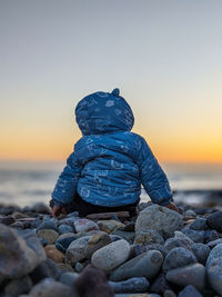 Rear view of man standing at beach against clear sky during sunset