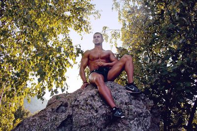 Portrait of shirtless man sitting on rock