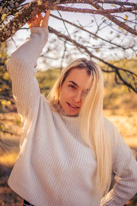 Portrait of young woman with arms raised standing against sky