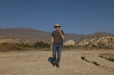 Adult man in cowboy hat on tabernas desert with palm trees against blue sky. almeria, spain