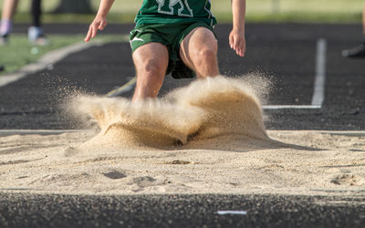 Full frame close-up view of an athlete landing in the sand pit at the end of his long jump