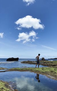 People standing on rocks by sea against sky