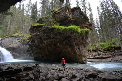 Woman standing by stream flowing in forest