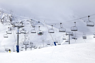 Ski lift over snow covered mountains against sky