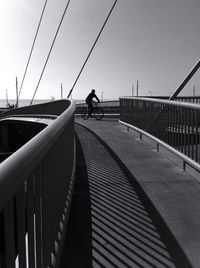 Man riding bicycle on footbridge against sky