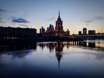 River and buildings against sky at dusk