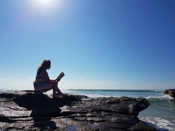 Side view of woman sitting on rock by sea