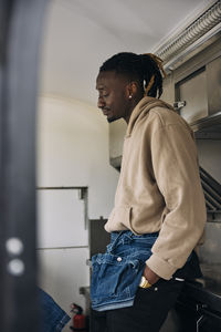Young man standing with hand in pocket seen through door of food truck