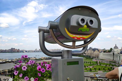 Close-up of coin-operated binoculars by building against cloudy sky