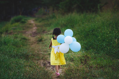 Rear view of girl with balloons walking on field