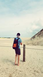 Rear view of boy standing on desert against sky