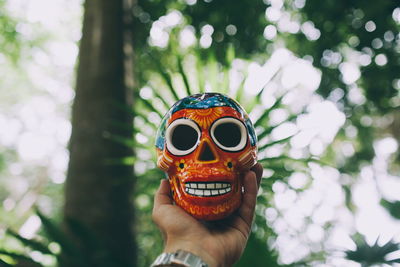 Close-up of hand holding skull against trees