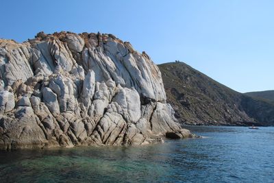 Scenic view of rocks by sea against clear sky